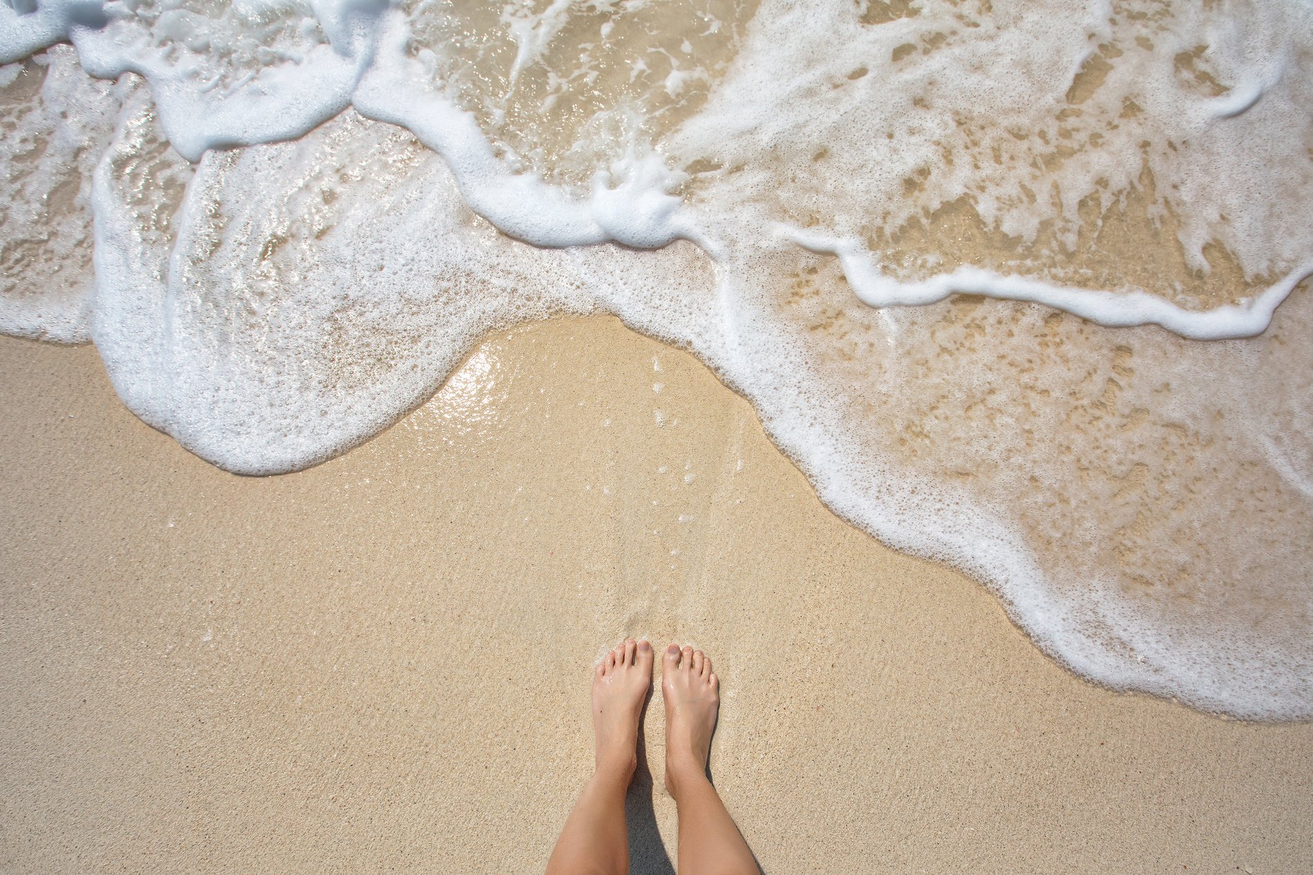 Vacation on ocean beach, feet on sea sand